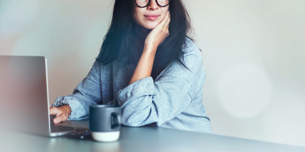Mulher sentada em mesa com café na frente do computador